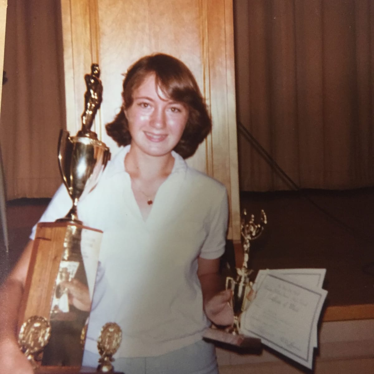 Teenage me holding a bunch of trophies and certificates